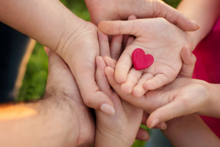 Hands of a child holding a red cloth heart with family's hands underneath