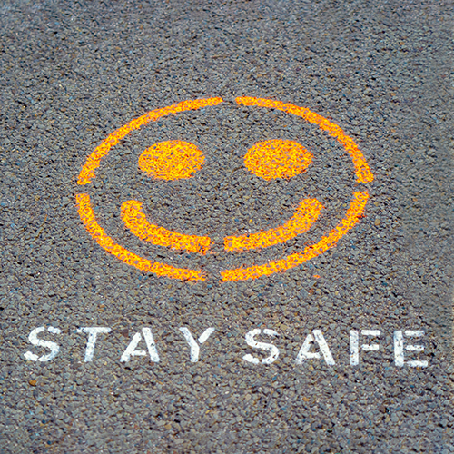 image of asphalt ground outside with a smiley face and the words "stay safe" painted on it