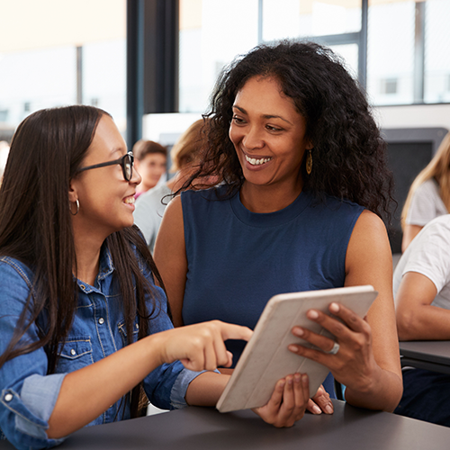 Image of an adult woman holding an electronic tablet and talking to a younger student girl as she points at the tablet