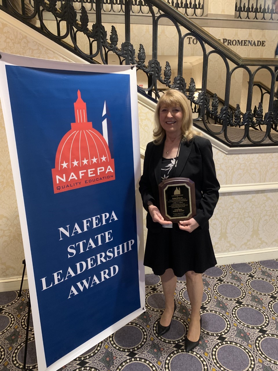 woman holding award standing next to NAEFPA step and repeat