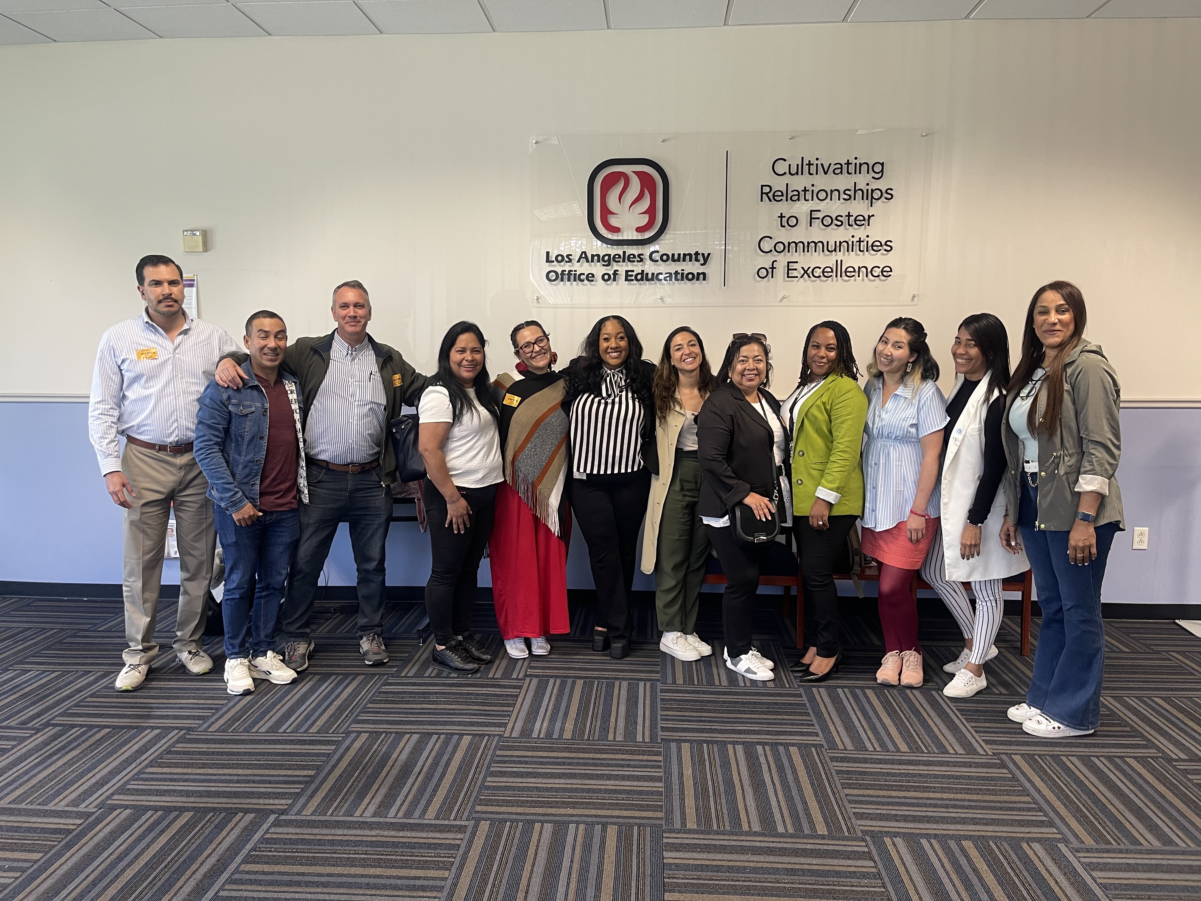 Guests pose with LACOE's Mental Health and School Counseling team in front of LACOE logo
