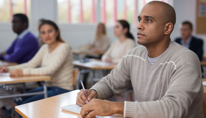 A man sits in classroom and takes notes