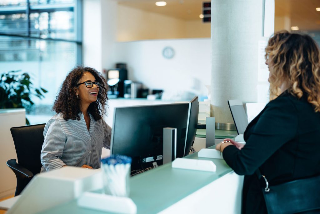 Receptionist assisting a woman standing at front desk.
