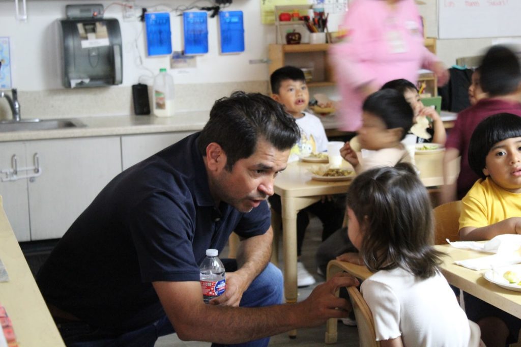 Rep. Gomez talking to a Head Start student in a classroom during lunch time