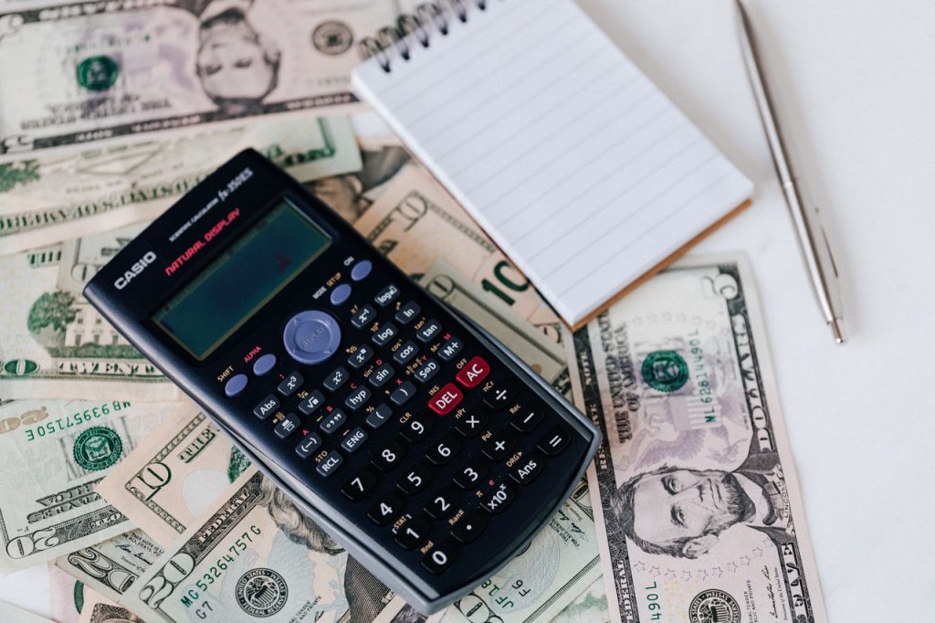 calculator on top of money next to a writing pad and pen