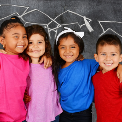 Young students smiling in front of a chalkboard with drawn graduation caps 