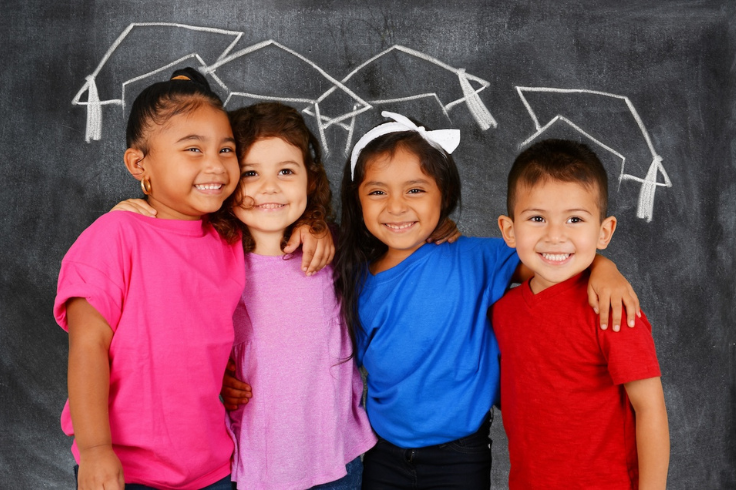 Young students smiling in front of a chalkboard with drawn graduation caps 