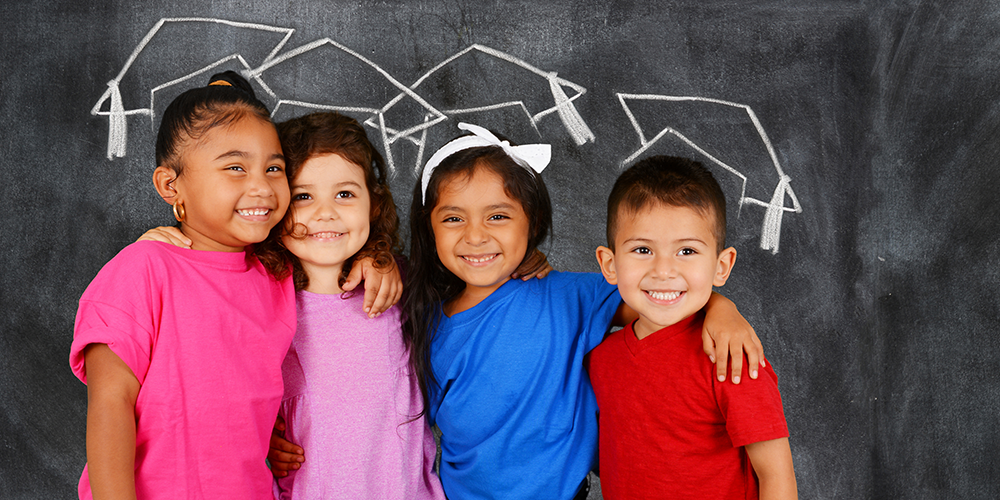 Young students smiling in front of a chalkboard with drawn graduation caps 