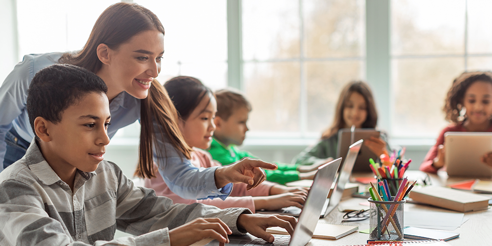 Teacher helping a student on a laptop
