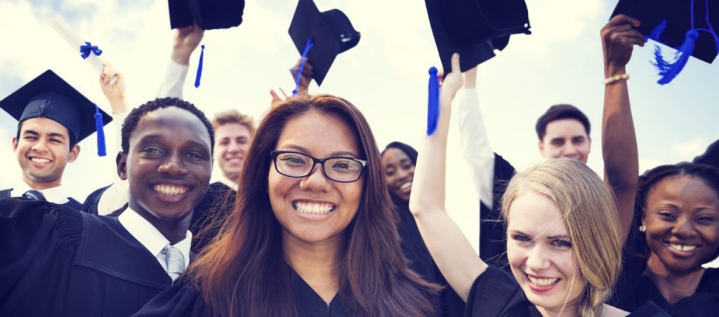 students in graduation gowns throwing caps