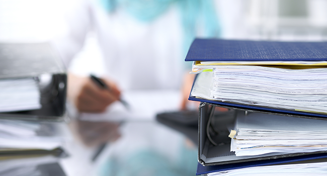 A person writing something surrounded by binders of paperwork