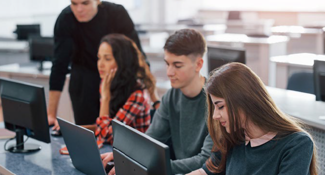 group of students using computers and laptops in a classroom setting